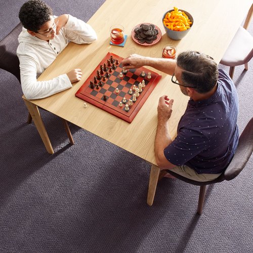 Two people playing chess at a wooden table in a room with purple carpet from Southwest Floors in Seven Hills, OH
